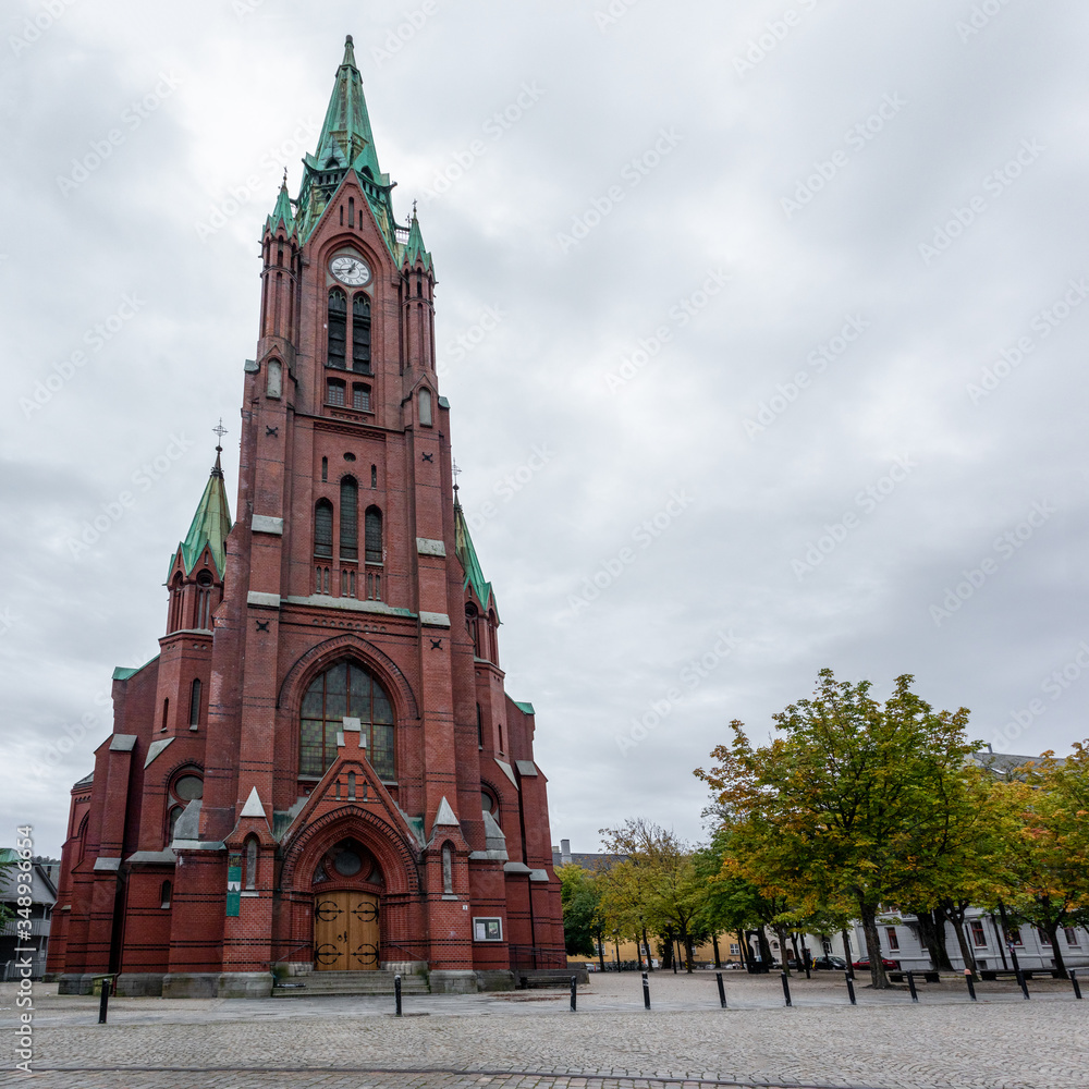 Fototapeta premium Panoramic view of high St. John's Church (Johanneskirken) in Bergen, Norway. Gothic-revival church with red brick & copper details. Cloudy autumn day city tourism