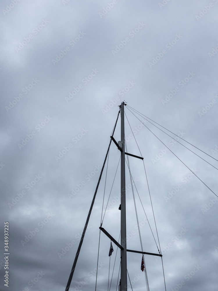 Sailing ship mast on heavy dark grey cloudy stormy sky background. Vertical close-up view Sailing ship mast on heavy dark grey cloudy stormy sky background. Vertical close-up view