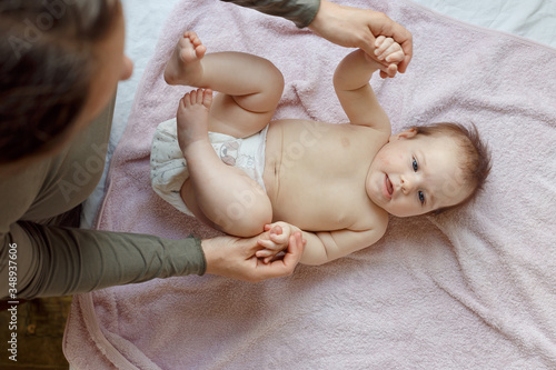 Top view of mother and her cute child on bed. Baby massage and exercises of gymnastics.