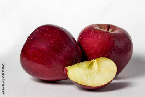 Two apples lie on a white background. Nearby lies an apple slice