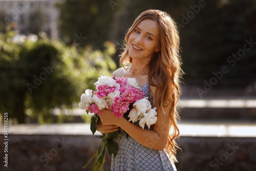 The model smiles and holds in her hands a bouquet of peonies flowers. sunset in the city for a walk. blurred background, concept