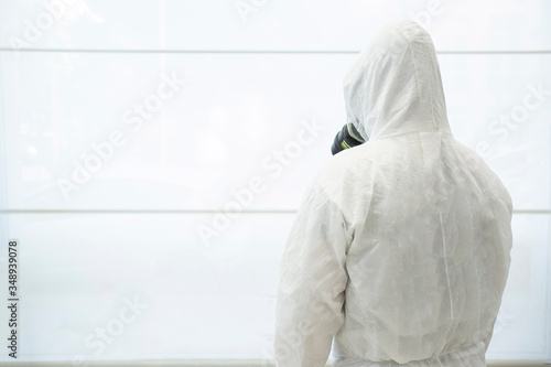 Tecnico per la Sanificazione dei locali e degli ospedali con tuta e maschera protettiva professionale, isolato su sfondo bianco  ripreso da dietro
 photo