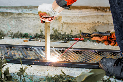 Welder connecting steel expanded (plain) sheet  and rolled metal rectangular pipe. Worker with weld equipment constructing fence of profile pipes and metal mesh grills. Metalworking and welding  