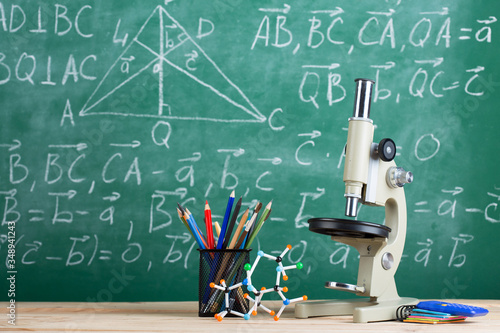 Education and sciences concept -molecule model and microscope on the desk in the auditorium, chalkboard background.