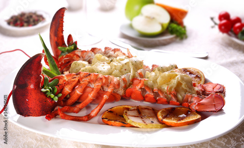 Baked lobster with applesauce and grilled bbq fruit on a white plate in a restaurant.