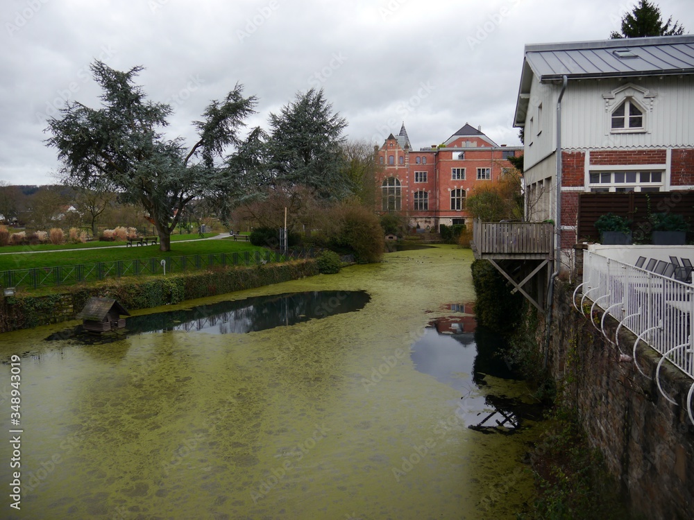 Pond overgrown with duckweed in snowless winter, parks on the right, idyllic old houses in the historic town of Kettwig on the left