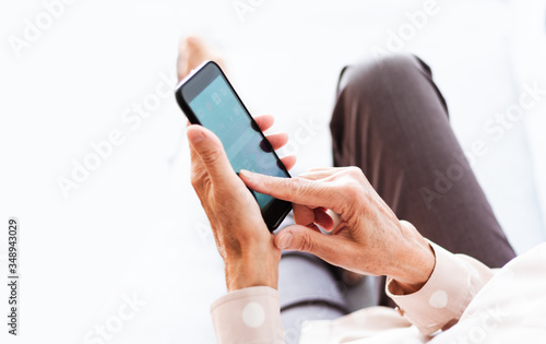 Middle-aged brunette woman on the gray sofa use mobile phone smartphone, surf internet.