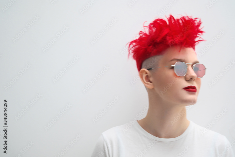 Portrait of a cool fashionable modern young girl. A short haircut with shaved temple. Dyed bright red hair. Red lipstick. Studio photo on white background. Suspenders and checkered pants. Portrait of a cool fashionable modern young girl. A short haircut with shaved temple. Dyed bright red hair. Red lipstick. Studio photo on white background. Suspenders and checkered pants.