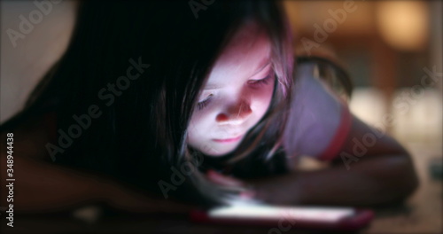 Child looking at cellphone screen at night. Little girl lying on floow staring at smarthone light.