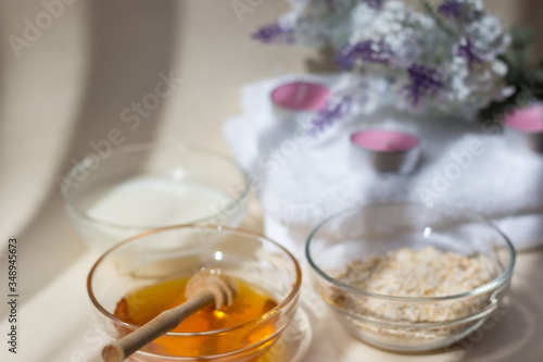 Home Spa skin care ingredients. Glass jars of oatmeal and yellow honey, a white towel for the bathroom. There is a lavender flower in the background. Side view. Sunlight. Dripping honey.