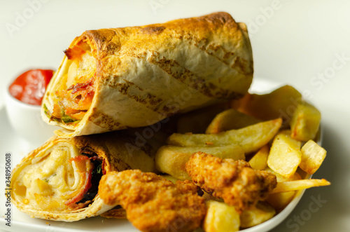 Tortilla wrap with chicken and beechwood smoked bacon served with chicken nuggets and chips on the white plate photo