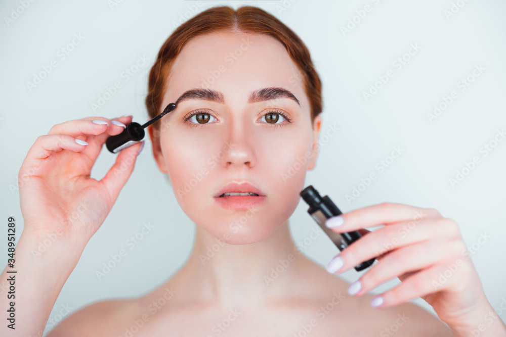 redheaded young woman looking natural applying brow mascara while doing makeup standing on isolated white background, makeup and beauty concept redheaded young woman looking natural applying brow mascara while doing makeup standing on isolated white background, makeup and beauty concept