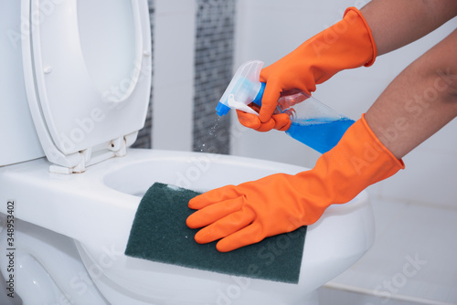 A woman hand wearing orange rubber gloves Cleaning toilet bowl with spray and scrub the dirt To prevent infection From public