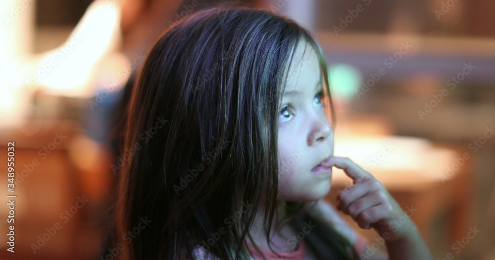Little girl child watching TV screen at night. Small kid hypnotized