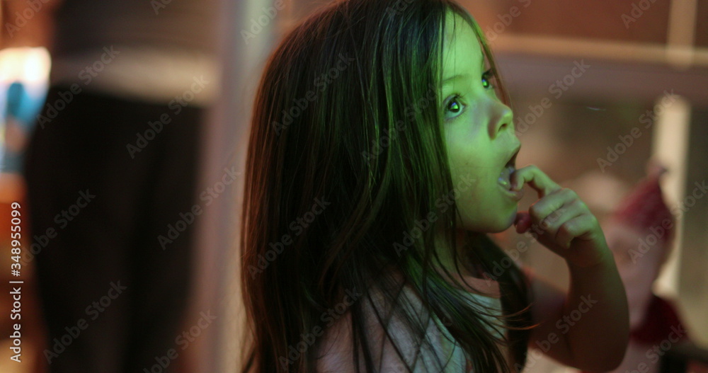 Little girl child watching TV screen at night. Small kid hypnotized