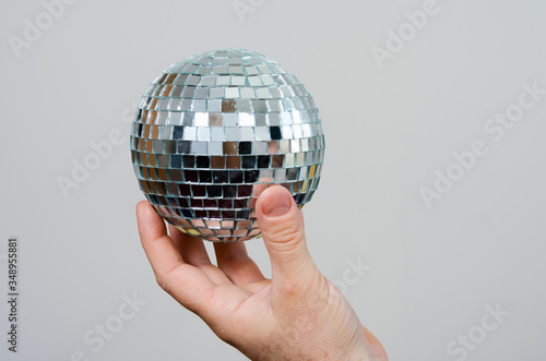 Close-up   hand of  a  man    holding  a  silver mirror  party  ball . Concept regarding parties after the covid-19 isolation period .