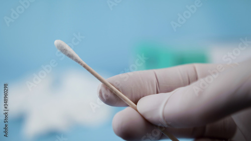 Close up of nurse with white gloves holding swab for coronavirus testing. Medical environment.