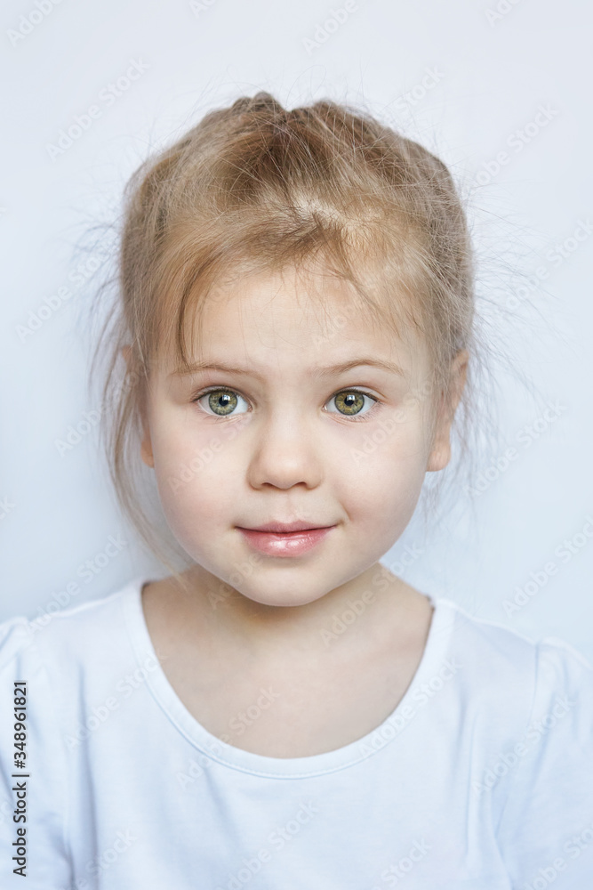 Portrait of a cute little Caucasian girl child with disheveled hair in a white t shirt on a light background