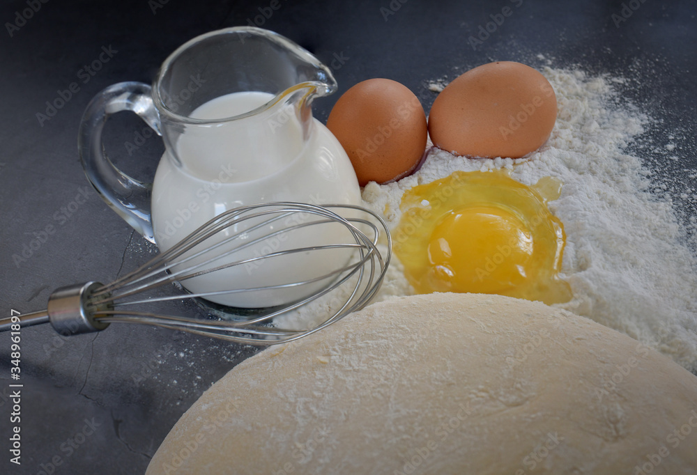 Appetizing still life of flour, eggs, a whisk, a jug of milk and dough