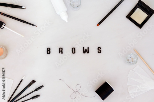 Brow beauty background in a flat lay style with treatment tools, eyebrow makeup and products arranged to create a frame for the word Brows.  Black text on a white background photo
