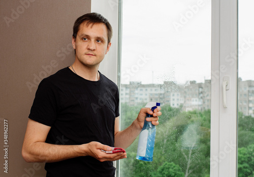 young guy in holds window cleaner and rag and washes plastic windows