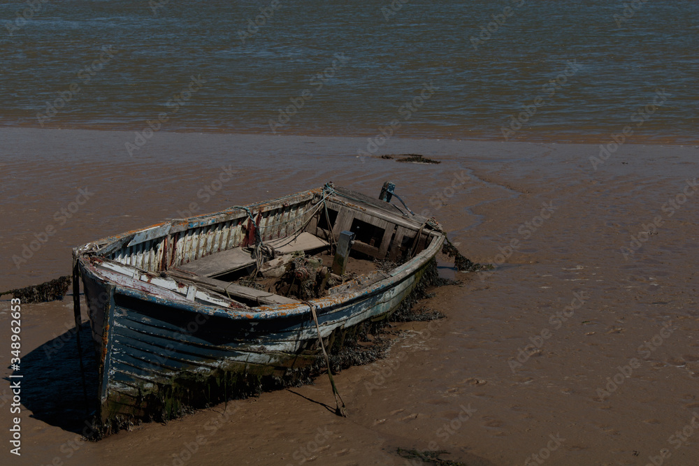 Rotting boat embedded into a beach with the water receding into the background Rotting boat embedded into a beach with the water receding into the background