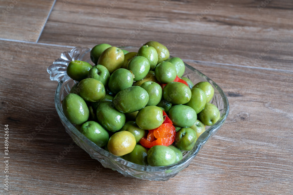 Green marinated olives with oregano, garlic, red pepper, herbs and spices on a wooden background. Recipe for marinated olives