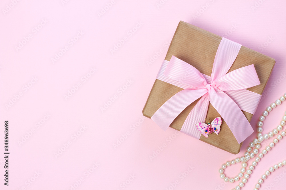 Gift box with a pink bow and pearl beads on a pastel pink background. Flat lay style. Gift box with a pink bow and pearl beads on a pastel pink background. Flat lay style.