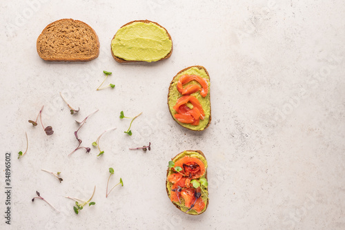 Stages of making a sandwich of bread, guacamole, salted salmon, baked tomatoes and greens
