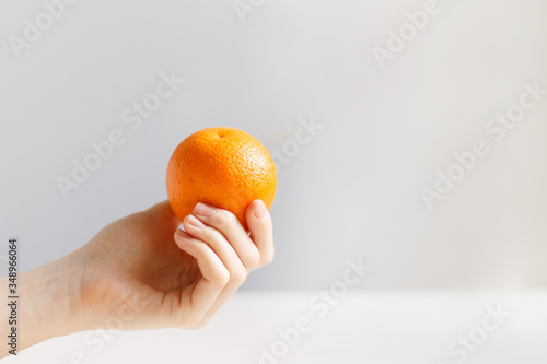 A hand holds an orange on a light background close-up. Orange in the hand.