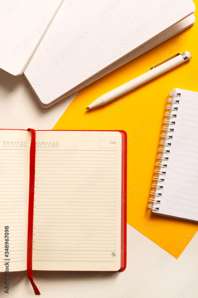 Business composition. Red open diary on a yellow background with notebooks and a white pen close-up. View from above. Flat lay. Business composition. Red open diary on a yellow background with notebooks and a white pen close-up. View from above. Flat lay.