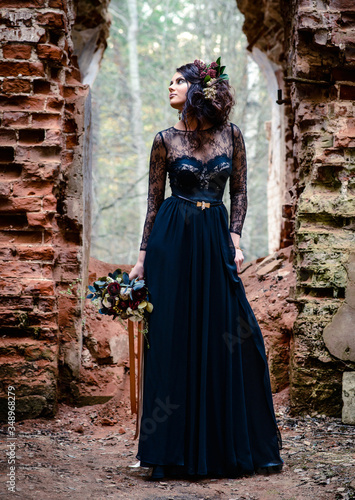 A mystical model in a black dress under an arch against the background of ruins. Black magic, Gothic beauty, halloween, black widow