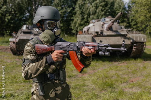 A soldier in a gas mask with a Kalashnikov rifle against the background of armored vehicles.