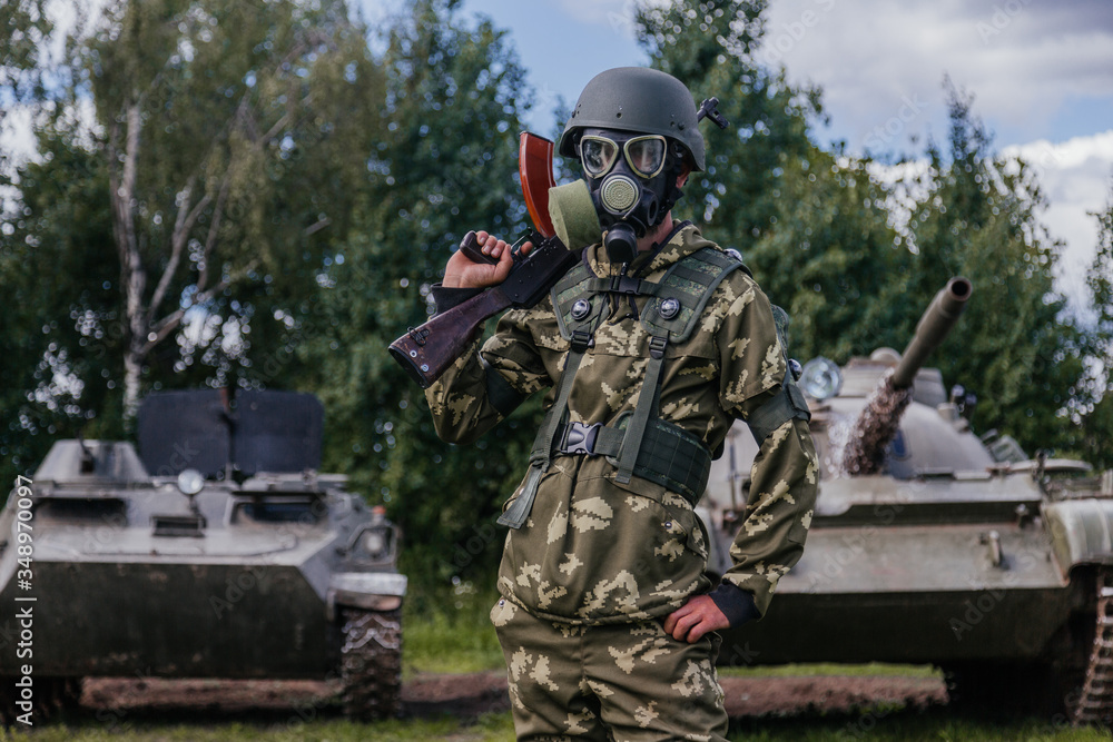A soldier in a gas mask with a Kalashnikov rifle against the background of armored vehicles. A soldier in a gas mask with a Kalashnikov rifle against the background of armored vehicles.