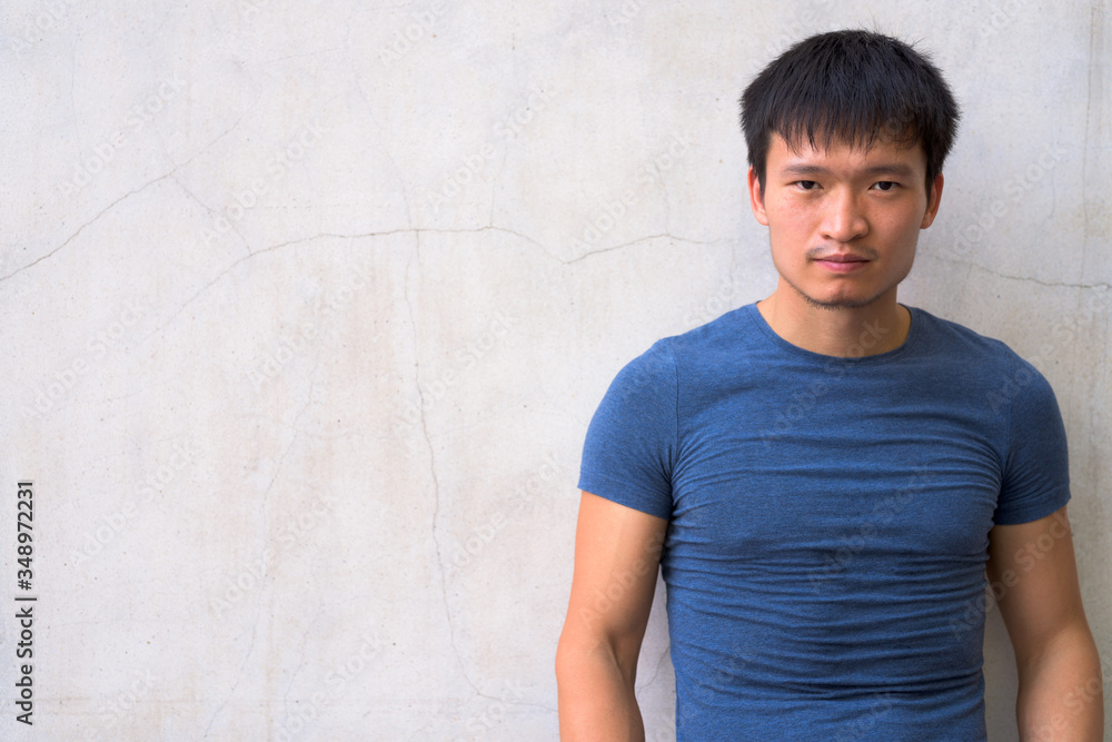 Portrait of young Asian man against concrete wall Portrait of young Asian man against concrete wall