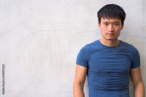 Portrait of young Asian man against concrete wall
