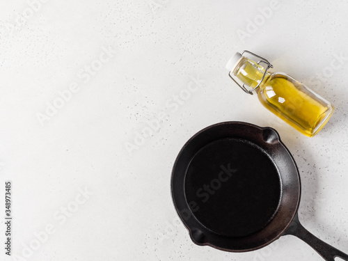 Fresh vegetable yellow oil in a glass bottle and black cast-iron frying pan on light background. Top view. Copy space