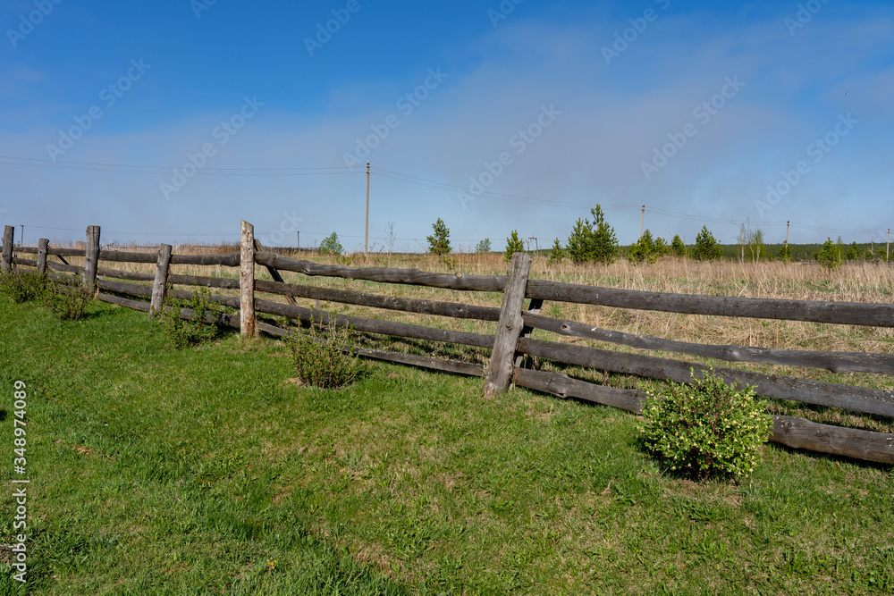 Picture of a rural lanscape with old rickety wooden fence, little green bushes, grass and blue sky at spring