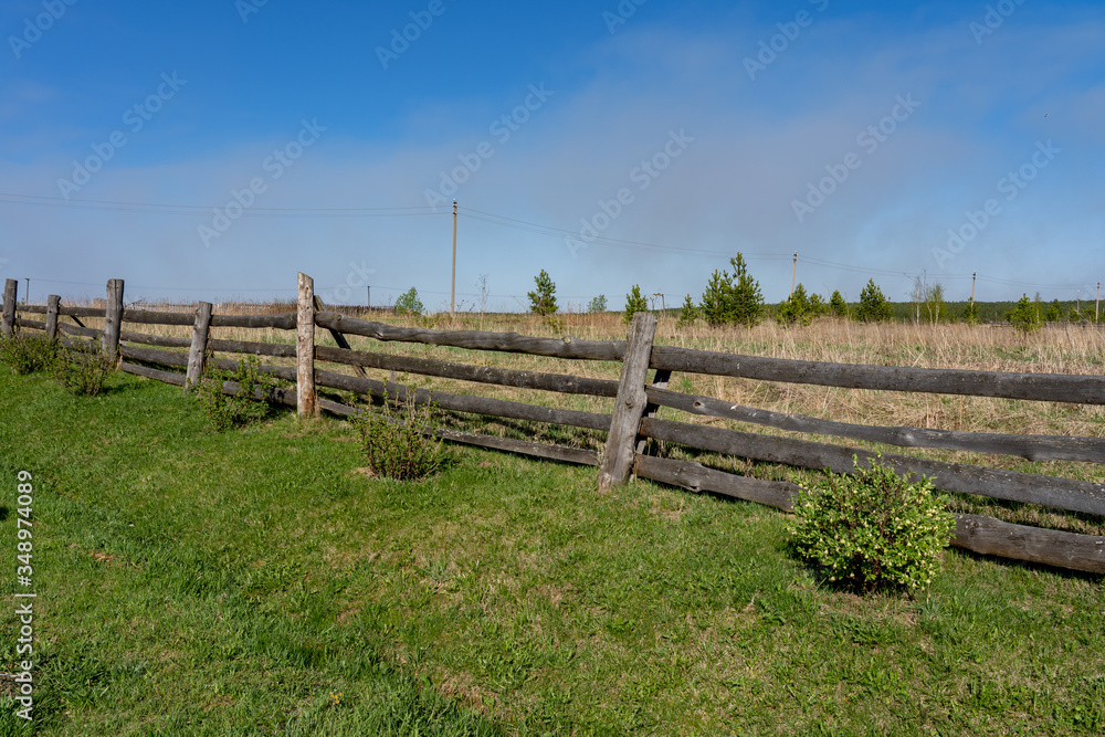 Picture of a rural lanscape with old rickety wooden fence, little green bushes, grass and blue sky at spring Picture of a rural lanscape with old rickety wooden fence, little green bushes, grass and blue sky at spring