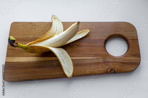 Side view of a yellow banana with peeled off skin which is laying on a white surface against background of white ceramic tiles