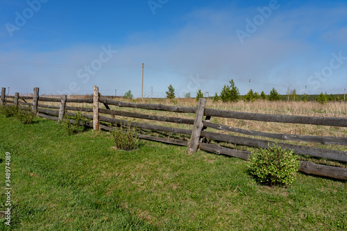 Picture of a rural lanscape with old rickety wooden fence, little green bushes, grass and blue sky at spring