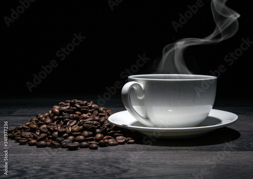 cup of hot coffee and roasted coffee beans on a wooden table on a black background