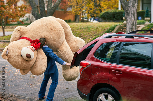 High angle shot of a man grabbing a valentines day gift out of the trunk of his car, surprising his partner with a large teddy bear.