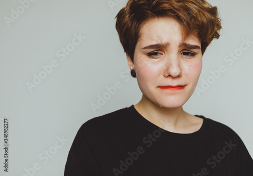 Girl with short hair cries on a white background