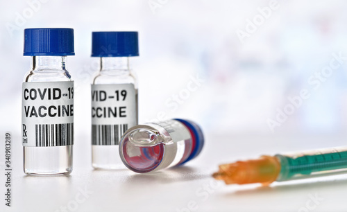 Coronavirus Covid 19 vaccine concept - small glass vials with blue caps on white table, green orange syringe near closeup detail (own design - dummy bar code)