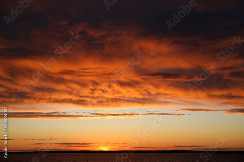 A fire is burning in the sky at sunset with lush illuminated orange clouds covering half of the clear horizon.The last glimmer near the lake.A striking contrast picture at the end of the day.Russia