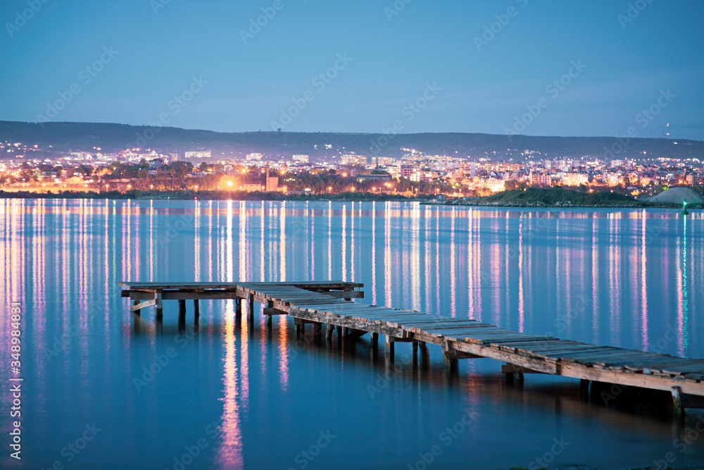 Empty Fishing pier at night with the city in the background with orange and teal