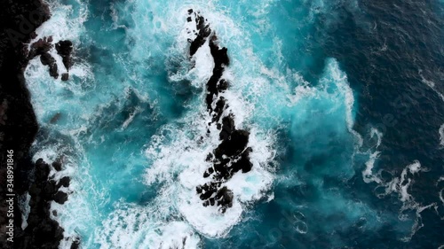 Aerial top down shot of big waves crashing into cliffs near the ocean shore of Porto Moniz, Madeira island, Portugal. Drone flying over blue turquoise water
