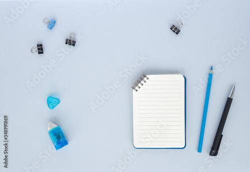 Flat lay with set of stationery: pen, pencil, copybook, notepad, eraser, paper clips on blue or gray background. Top view, copy space, monochrome. Back to school, education, office concept.