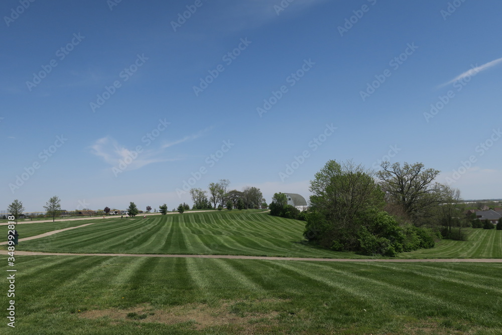 Grass Cutting Row Lines On Lightly Rolling Hills At Park With Barn In Distance
